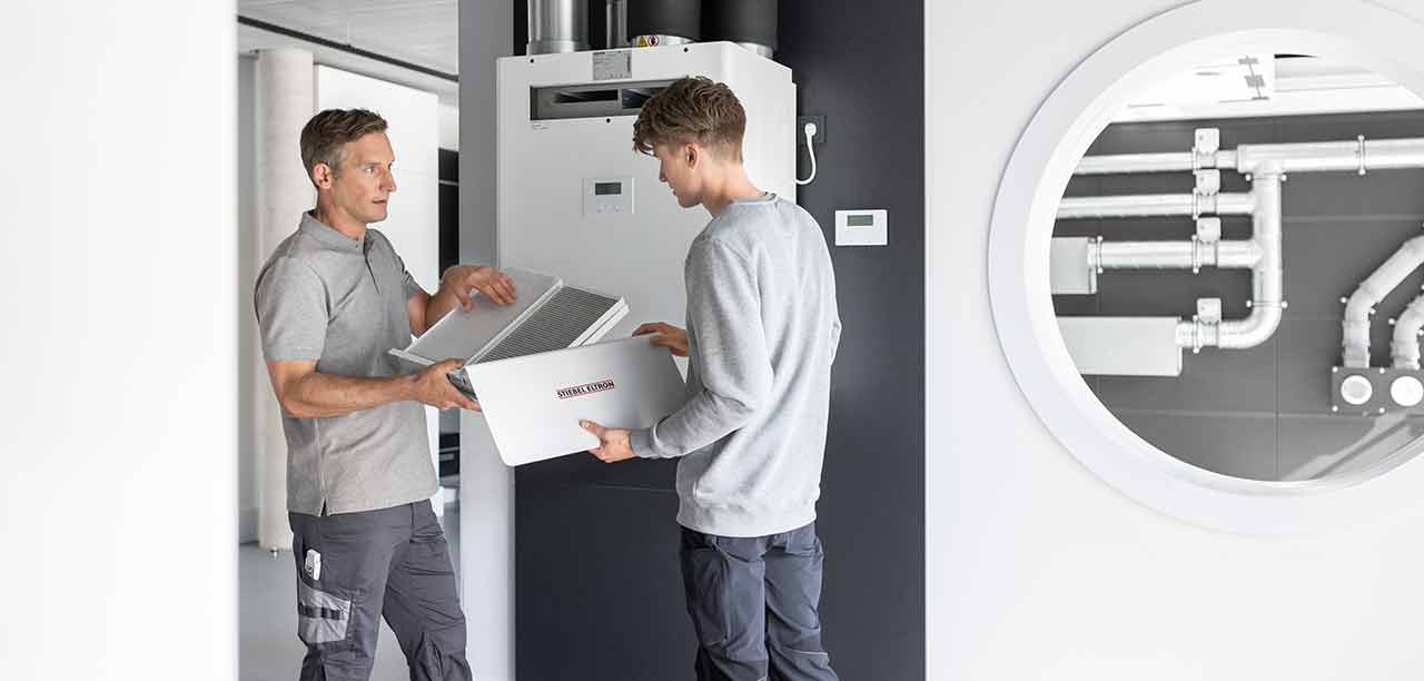 Zwei Auszubildende und ein Ausbilder vor einer Wärmepumpe von STIEBEL ELTRON